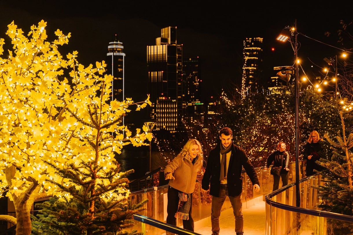 Two people holding hands on skate trail with London landscape in the background