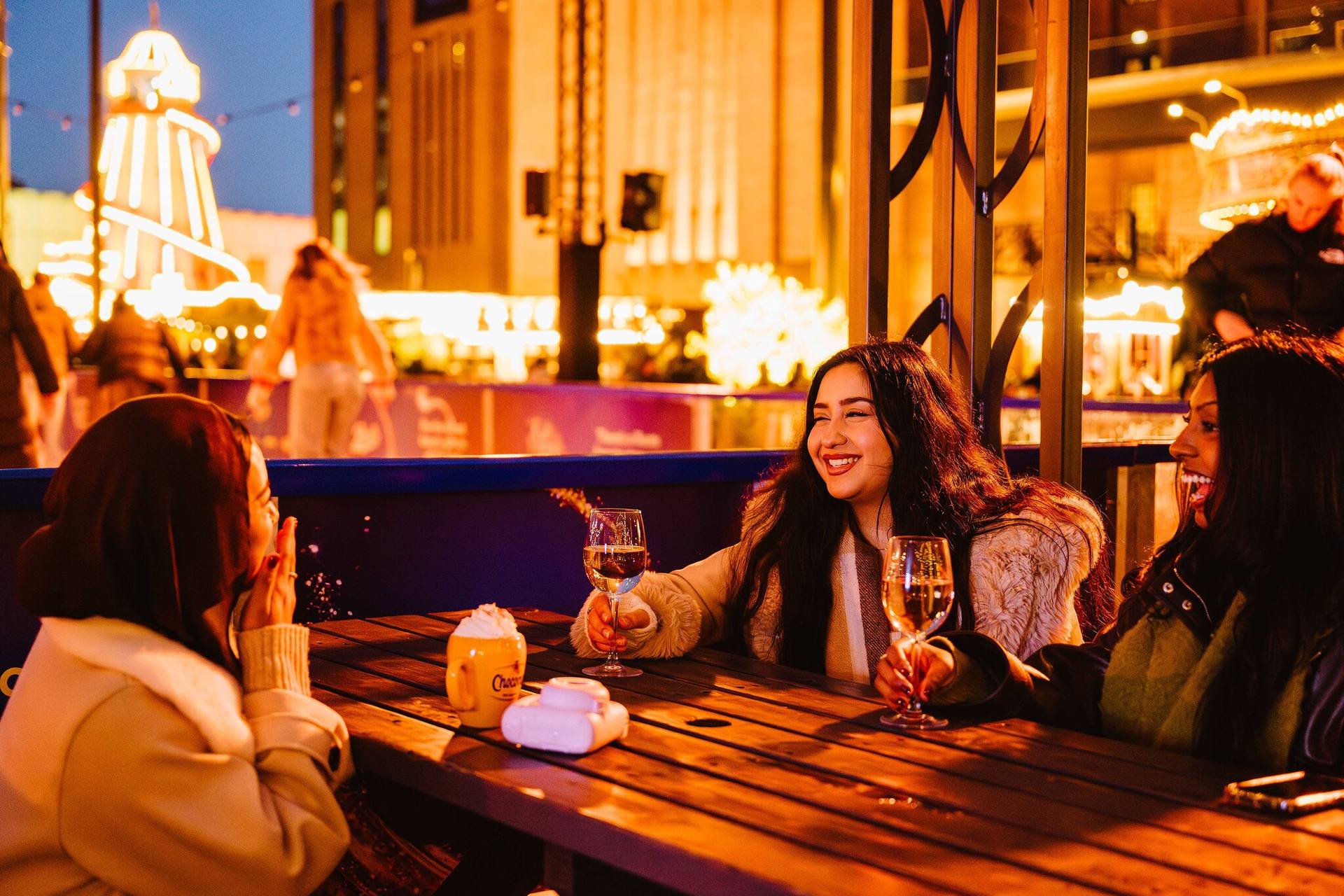 Friends laughing with drinks at the bar next to the ice rink